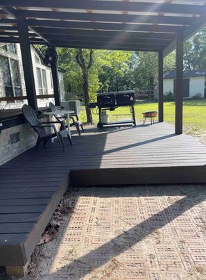 Eine überdachte Terrasse mit Grill, Sitzgelegenheit und Blick auf den umliegenden Garten.
