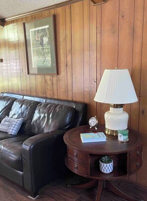 Ein Zimmer mit Holzwandverkleidung, einer Ledersofa, einem Tisch mit Lampe, einem gerahmten Bild und einer kleinen Uhr.