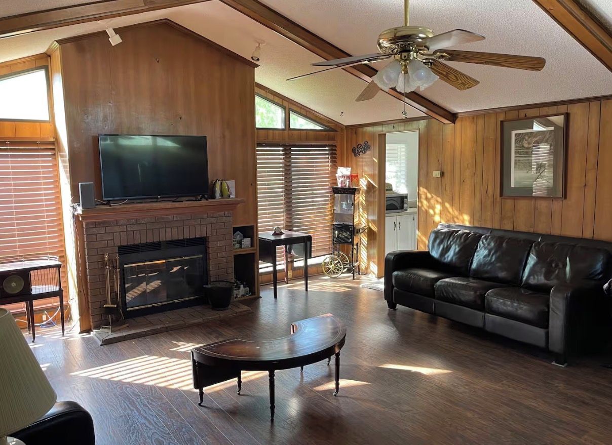 Una sala de estar con chimenea, televisor, sofá de cuero y ventilador de techo.