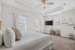 Una habitación de hotel con cama, cortinas, televisión y ventilador de techo.