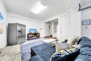 A living room with a sofa, a coffee table, a TV, and a refrigerator. - 🌴Blue Skies & Tail Winds | Private Pool | 4 Bikes | Private Beach Access🌴 (Destin)