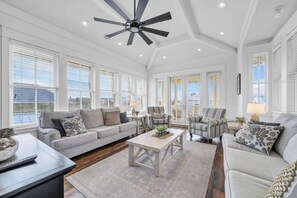 A spacious living room with a ceiling fan, large windows, and a fireplace. - 🌴Blue Skies & Tail Winds | Private Pool | 4 Bikes | Private Beach Access🌴 (Destin)