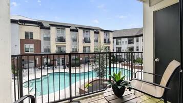 A balcony with a view of a swimming pool and adjacent buildings.