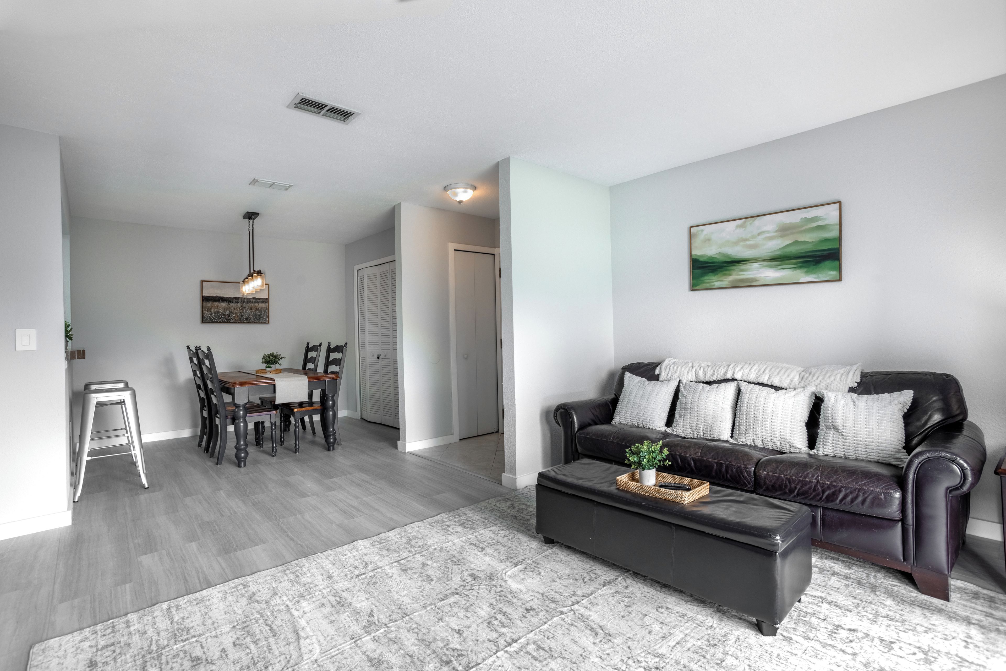 A modern living room with a black leather sofa, a dining table with chairs, and a hallway leading to a closet.