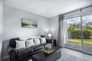 Una sala de estar moderna con un sofá de cuero, una mesa de centro con una planta, un cuadro en la pared y vistas a través de un ventanal.