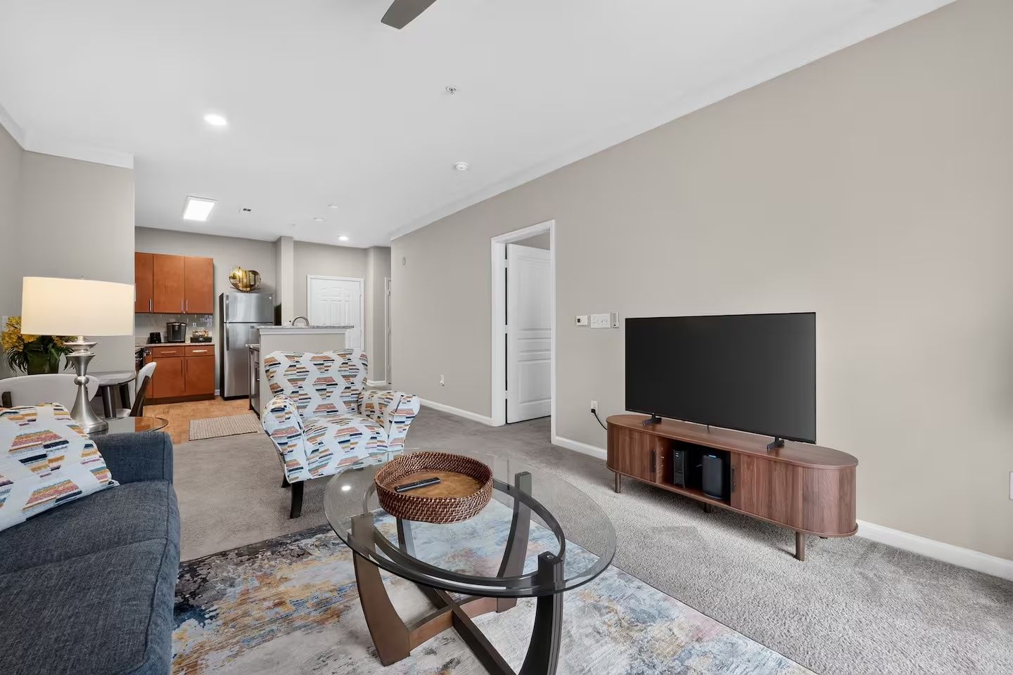 A modern living room with a flat-screen TV, a sofa, a coffee table, and a kitchen in the background.
