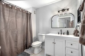 Un baño con inodoro, lavamanos y espejo, y cortina de ducha.