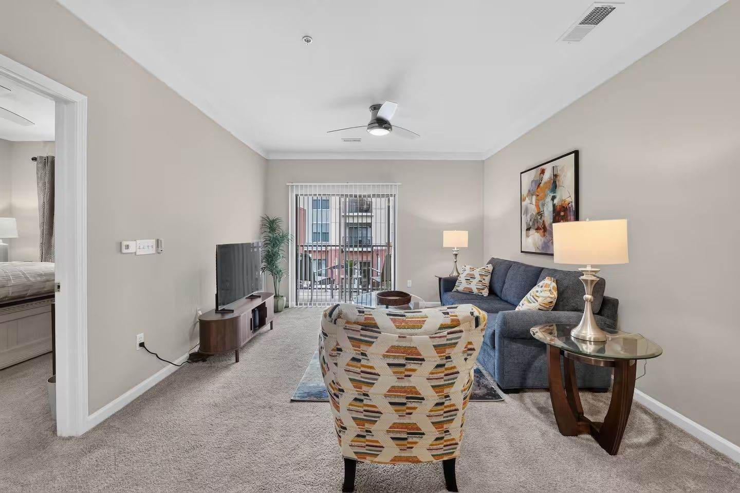 A living room with a TV, a patterned armchair, a sofa, and a lamp.