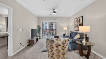 A living room with a TV, a patterned armchair, a sofa, and a lamp.