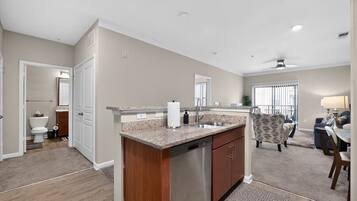 A modern kitchen with granite countertops, a dishwasher, and a dining area with a patterned chair and a table.