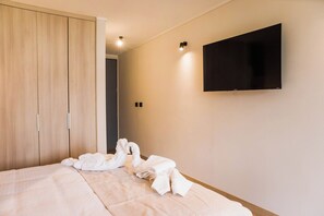 Ein Hotelzimmer mit einem Bett, einem Kleiderschrank, einem flachbildfernseher an der Wand und einem Paar Handtücher, die auf dem Bett drapiert sind.