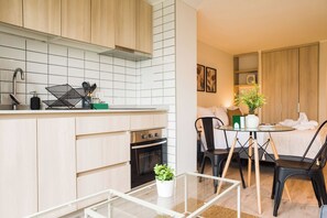A modern kitchen with a built-in oven, a dining area with a glass table, and a living space with a sofa and a plant. - Sunny Studio in Nunoa for 3 Guests (Ñuñoa)