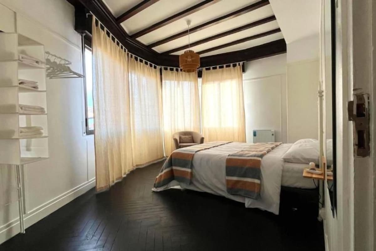 A bedroom with a bed, a chair, a wardrobe, and a window with curtains.