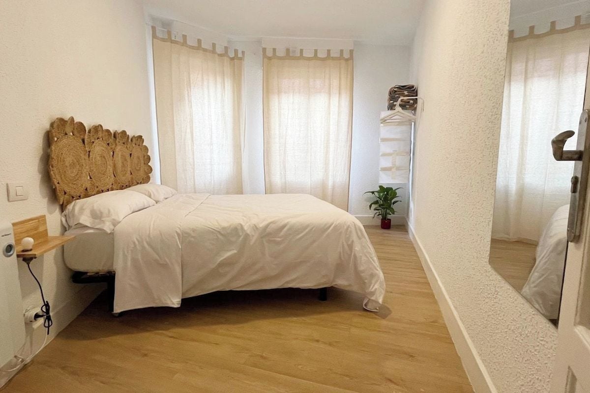 A bedroom with a bed, a wooden headboard, a bedside table, a potted plant, and a mirror.