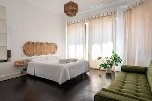 A bedroom with a bed, a green sofa, a potted plant, and a wall-mounted light fixture. - HT.Miribilla (Bilbao)
