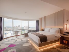Una habitación de hotel moderna con una cama grande, un escritorio, una silla y vistas a la ciudad.
