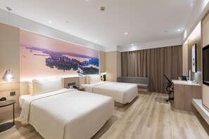 Habitación de hotel con dos camas, un escritorio, una silla, un televisor y un ventanal con vistas a un paisaje urbano.