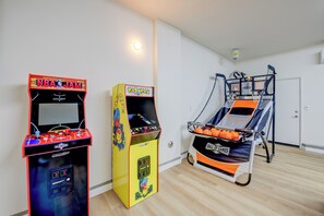 Ein Raum mit zwei Spielautomaten, einer mit der Aufschrift 'NBA JAM' und der andere mit 'PAC-MAN', sowie einem Basketballkorb.
