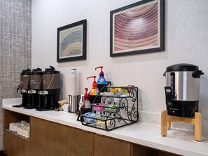 Un mostrador de desayuno de hotel con cafeteras, dispensador de agua y una jarra de café.