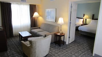 Une chambre d’hôtel avec un canapé, une petite table, une lampe, un lit et un sol recouvert de moquette.