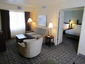 Habitación de hotel con sofá, una mesita, lámpara, cama y piso alfombrado.