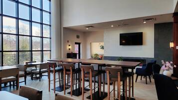 Een ruime binnenruimte met hoge plafonds, grote ramen en diverse zithoekjes, inclusief tafels en stoelen.