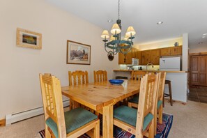 Ein Essbereich mit Holztisch und Stühlen, einer Chandelüster und einer Küche im Hintergrund.