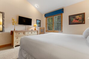 Een slaapkamer met een bed, een dressoir, een televisie, een raam met uitzicht op bomen en een schilderij aan de muur.