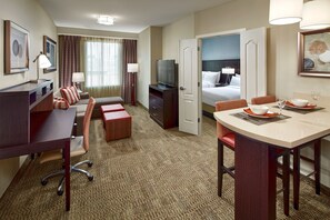 A hotel room with a desk, a sofa, a dining table, a TV, and a bed.