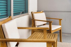 Zwei Holzsessel mit weißen Kissen, nahe an einem Fenster mit blauen Rolläden.