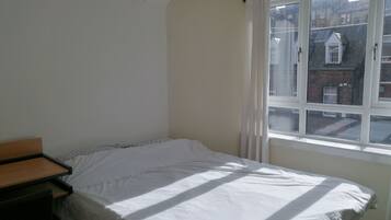 A bedroom with a single bed, a small bedside table, and a window with a view of buildings.