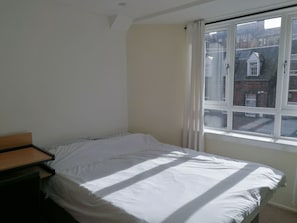 A bedroom with a single bed, a small bedside table, and a window with a view of buildings. - City Centre Apartment Free Parking (Glasgow)