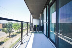 En balkon med bord og stole, store vinduer og udsigt til gaden.