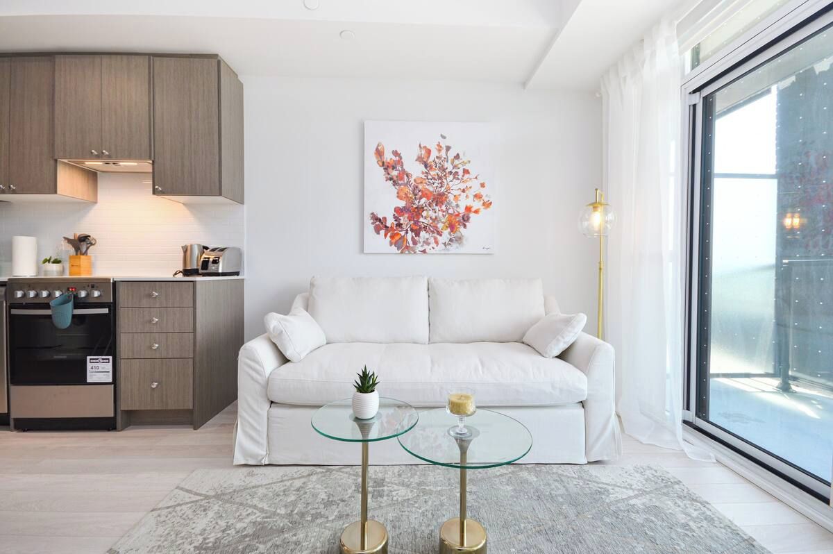 A modern living room with a sofa, a glass coffee table, and a kitchen area with cabinets and appliances.