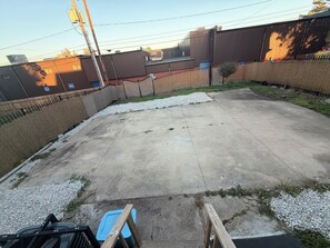 Un patio de hormigón con un contenedor azul, rodeado por una valla y grava.
