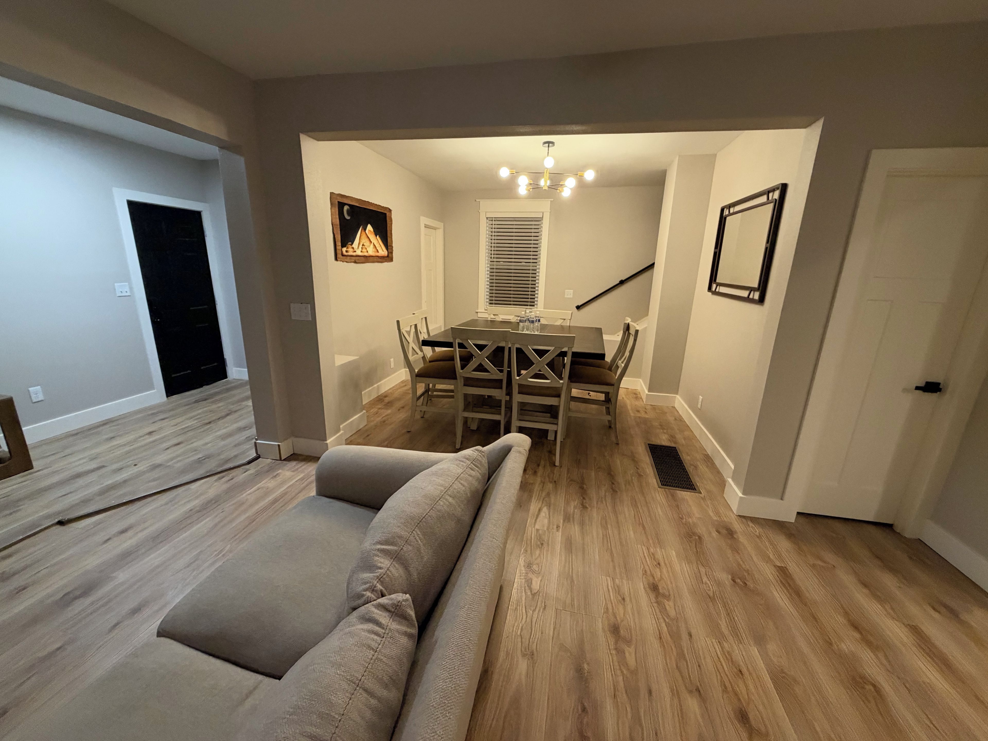 A dining area with a wooden table and chairs, a bench, a chandelier, and a staircase.
