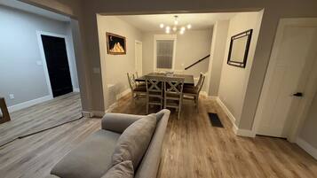 A dining area with a wooden table and chairs, a bench, a chandelier, and a staircase.