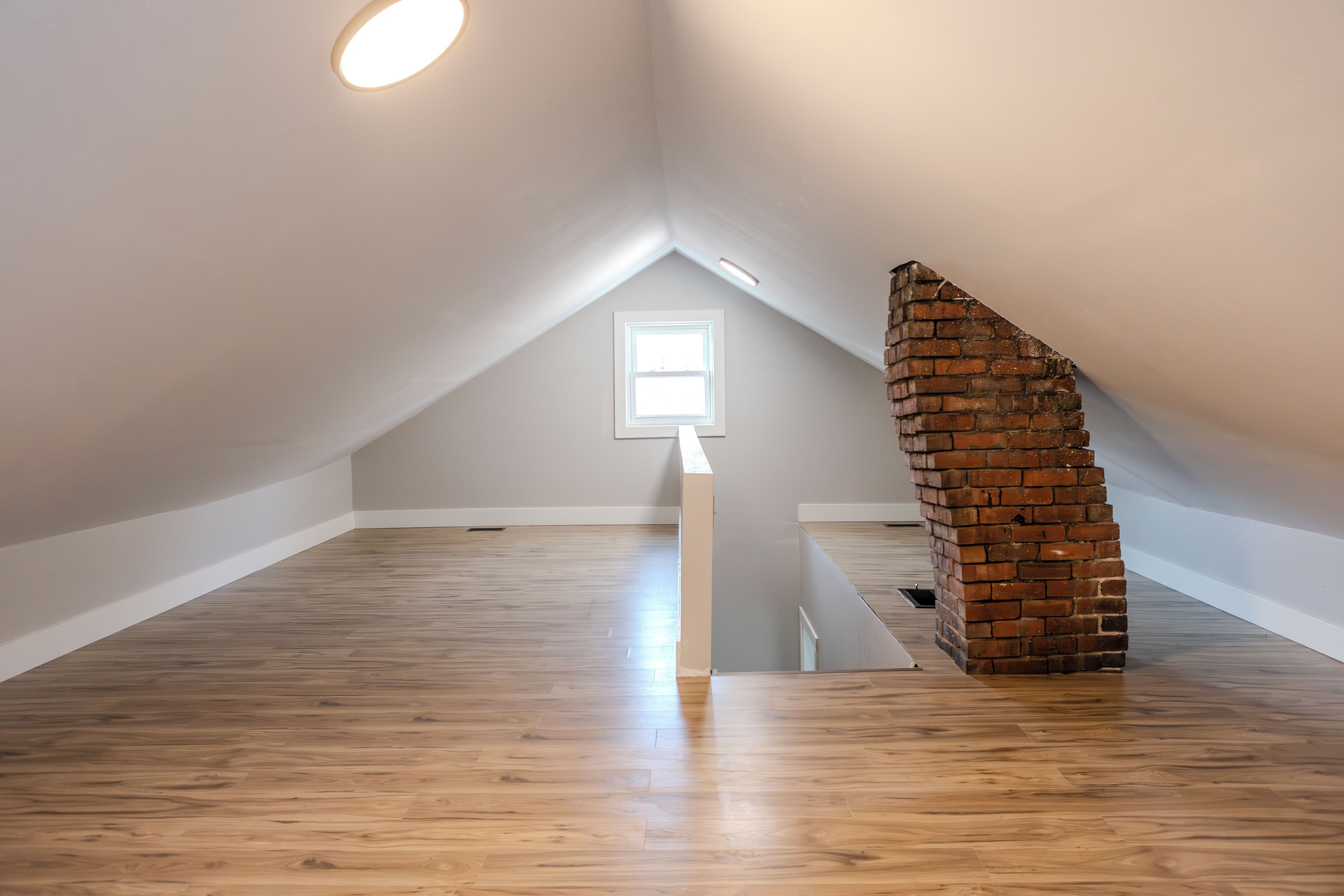 Ein Zimmer mit Holzboden, schrägen Decken und einer Ziegelstruktur.