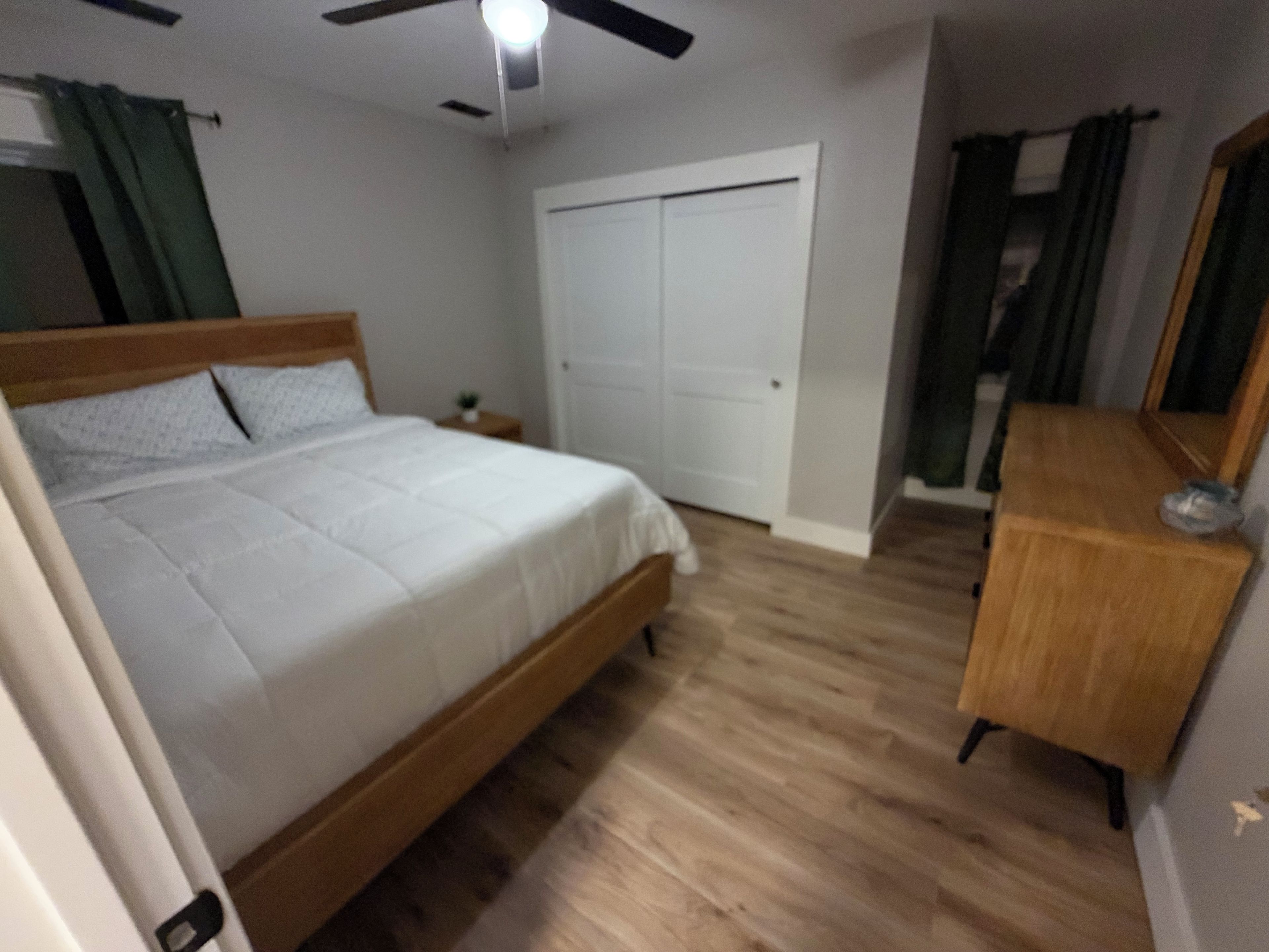 Une chambre à coucher avec un lit, une commode en bois, un ventilateur de plafond et une porte blanche.