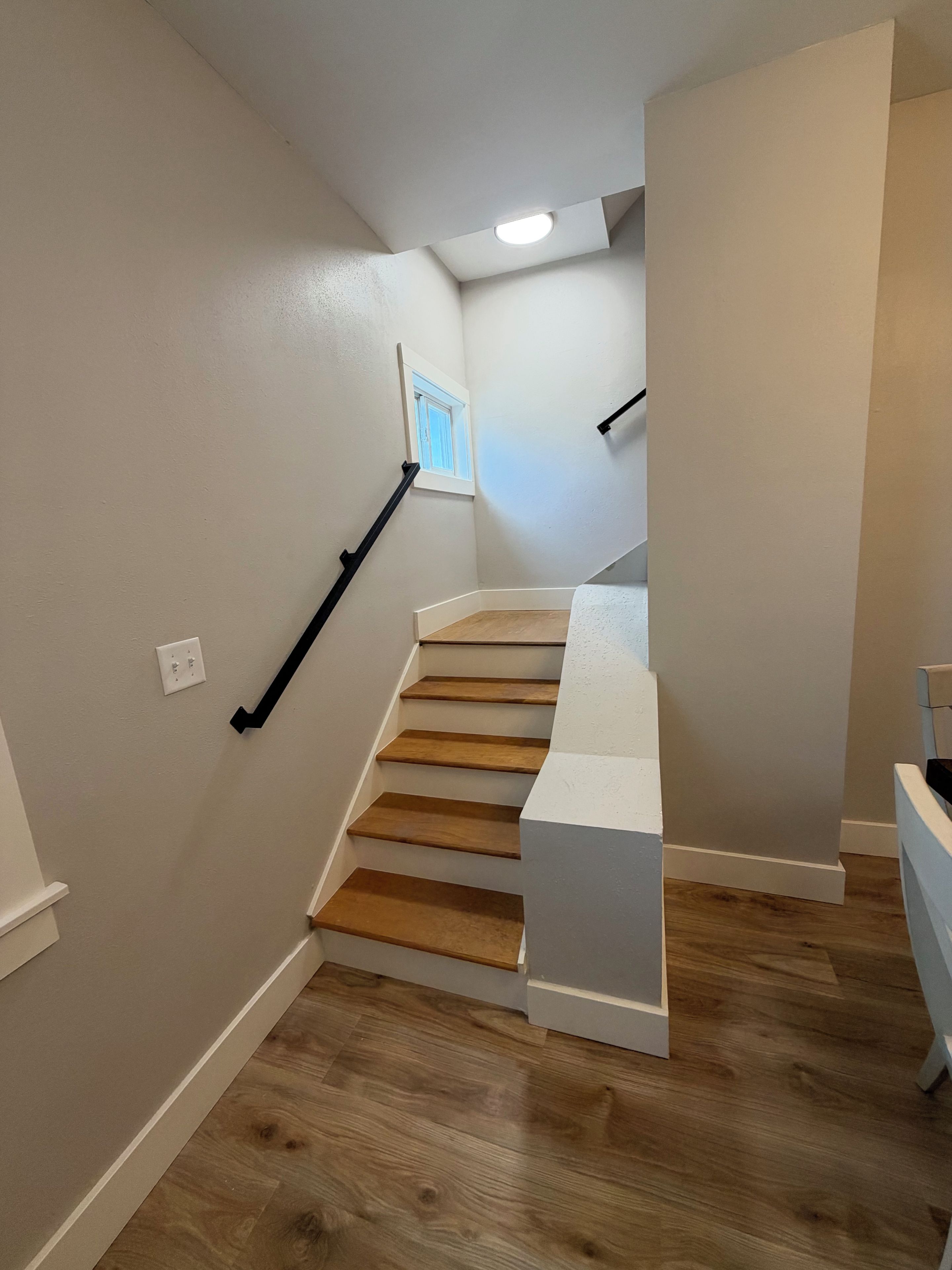 A staircase with wooden steps and white walls, leading to a landing with a small window.