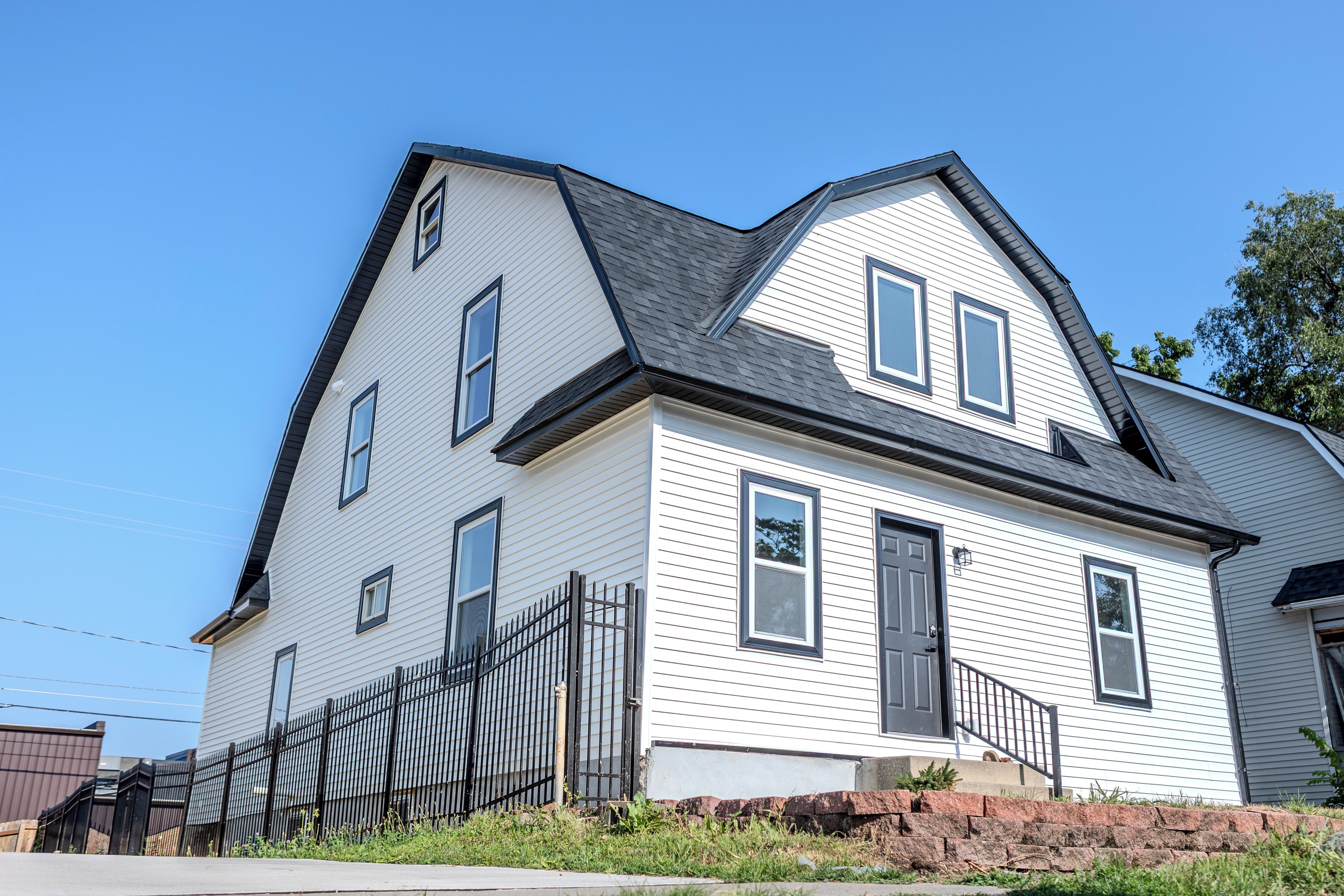 A two-story house with a gabled roof, a front porch, and a black metal fence.