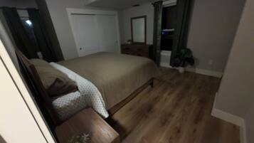 A bedroom with a bed, a wooden nightstand, a potted plant, and a ceiling fan.