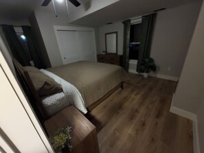 Un dormitorio con cama, mesita de noche de madera, planta en maceta y ventilador de techo.