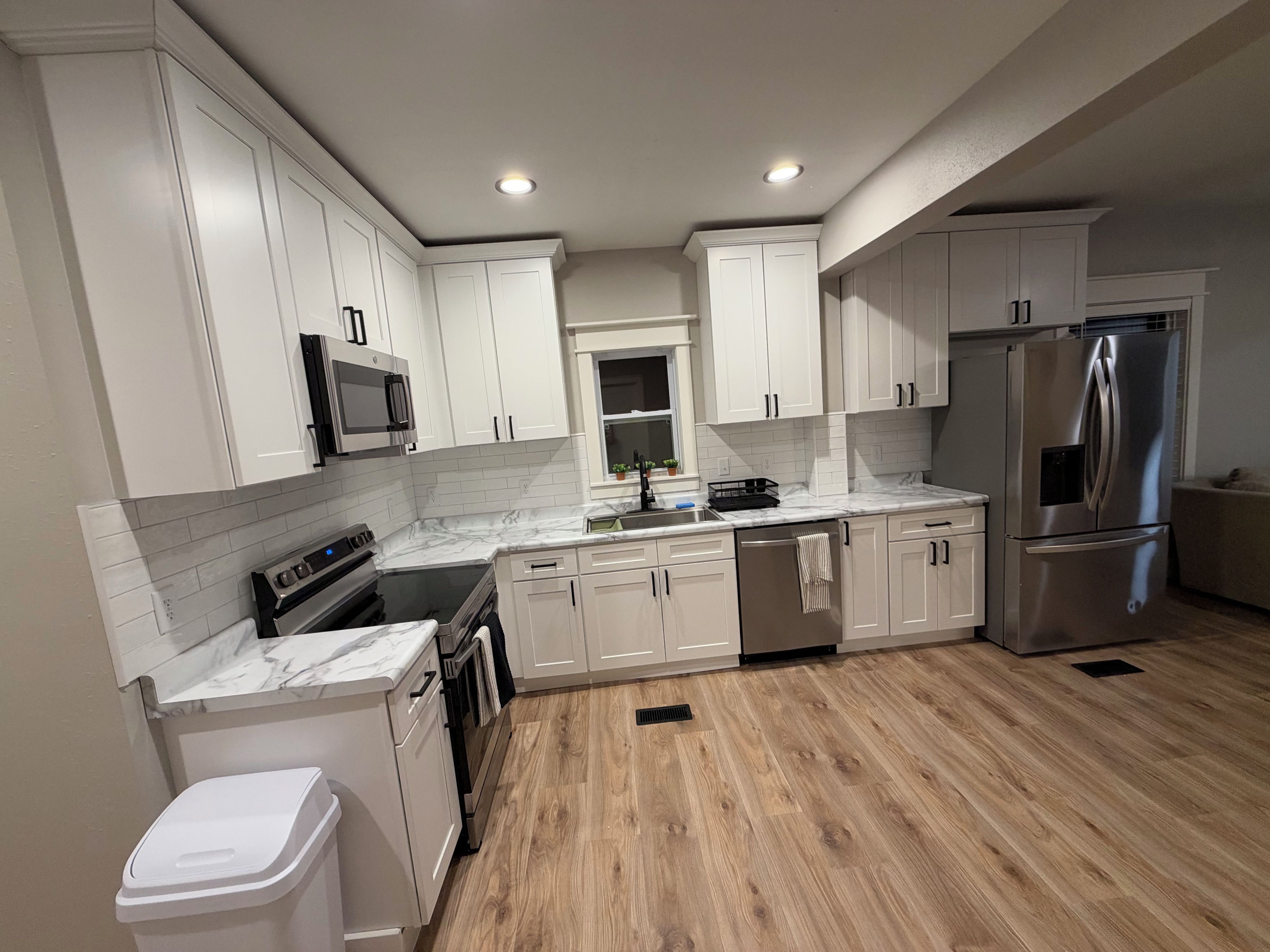 A modern kitchen with white cabinetry, stainless steel appliances, and a wooden floor.