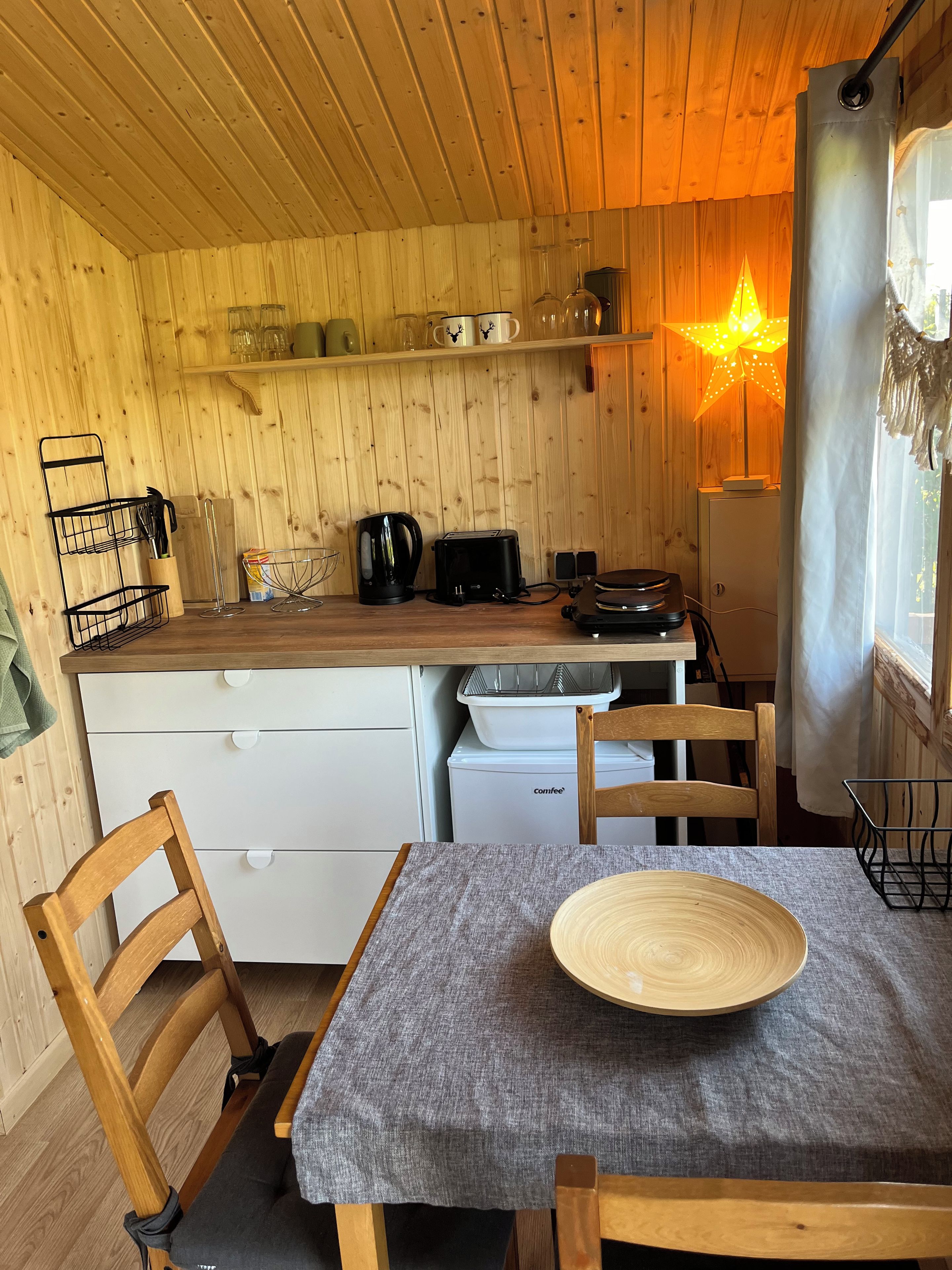 Uma cozinha acolhedora com paredes de madeira, uma mesa com um prato, cadeiras, uma cafeteira e uma geladeira.
