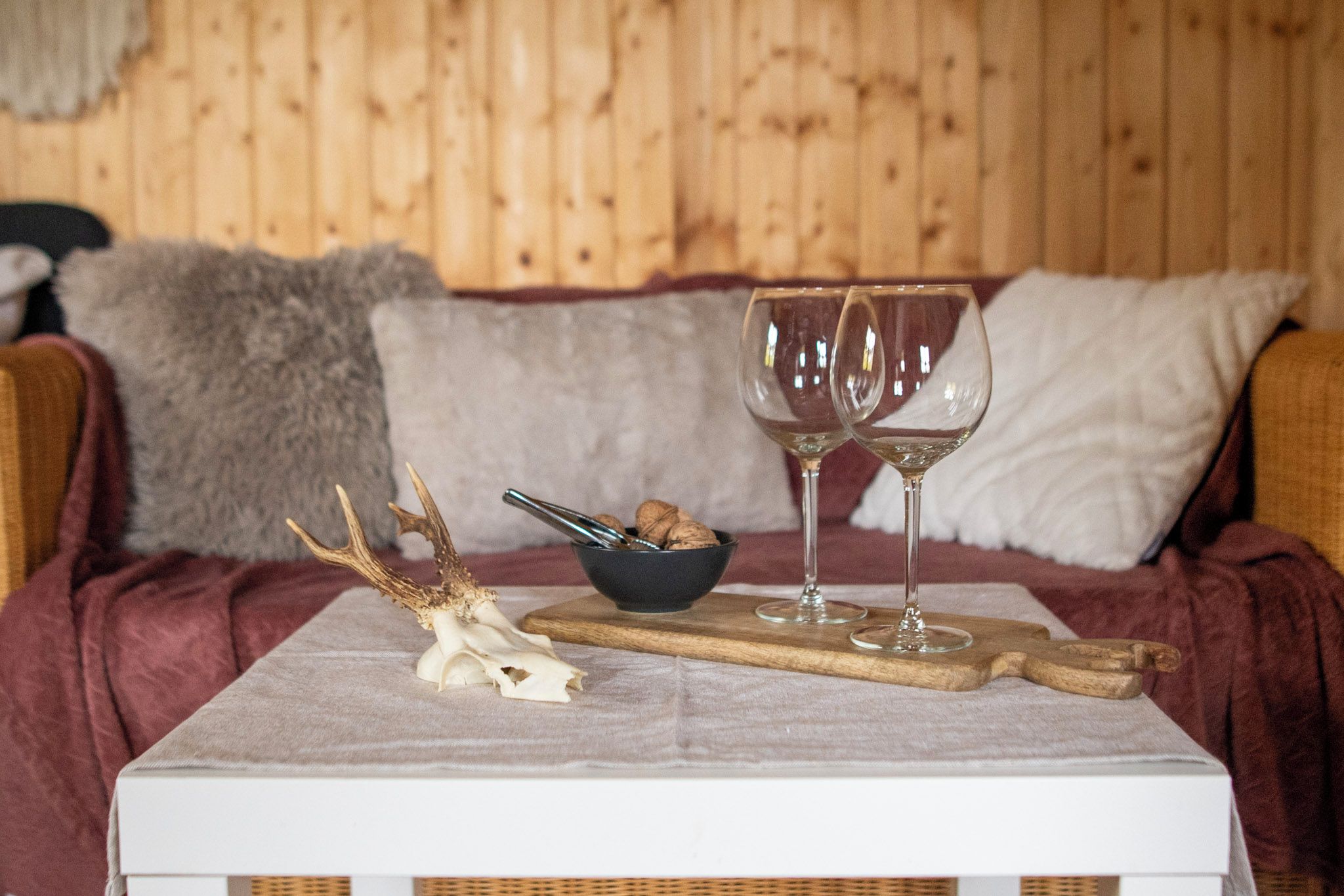 A wooden bed with a white headboard, a bowl of nuts, two wine glasses, and a deer antler on a white tray.