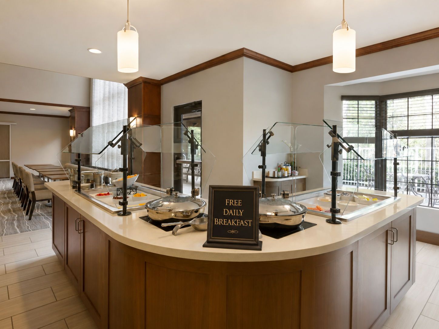 A breakfast bar with a sign offering free daily breakfast, equipped with multiple serving stations and overhead lighting.