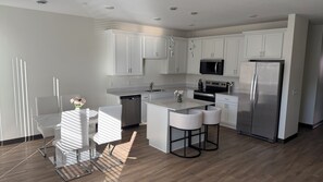 A modern kitchen with white cabinetry, stainless steel appliances, and a central island with bar stools. - #202-2-bedroom furnished modern Townhome - 2.5 mile from Mayo Clinic (Rochester)