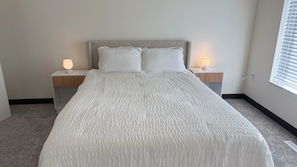 Ein Schlafzimmer mit einem Bett, zwei Nachttischlampen und einem Fenster mit Jalousien.