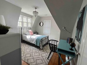 Un dormitorio con cama, escritorio, silla, ventana y candelabro.